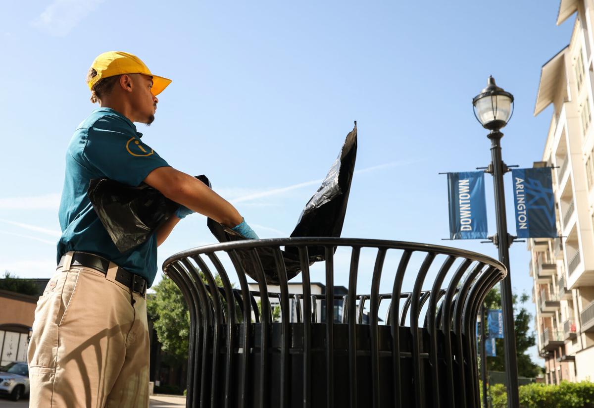 An Arlington Ambassador puts a trash bag into a trash can in Downtown Arlington, TX.