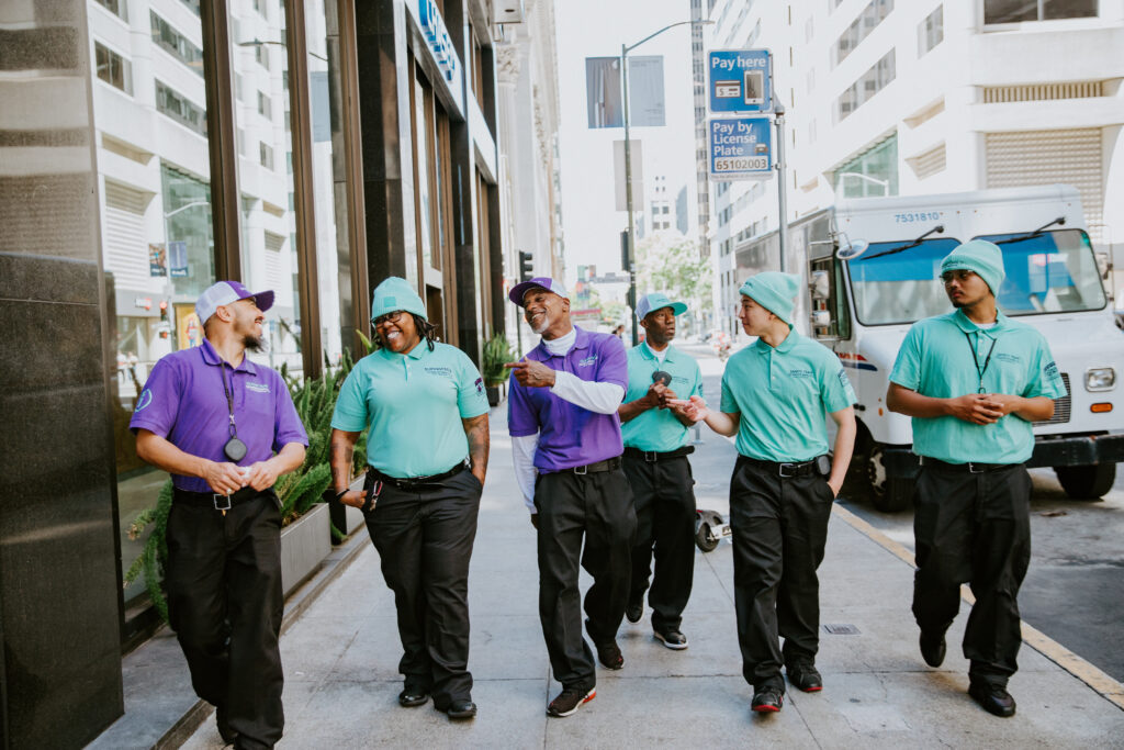 A group of Downtown San Francisco Partnership Ambassadors walk down the street together while wearing two matching. uniforms.