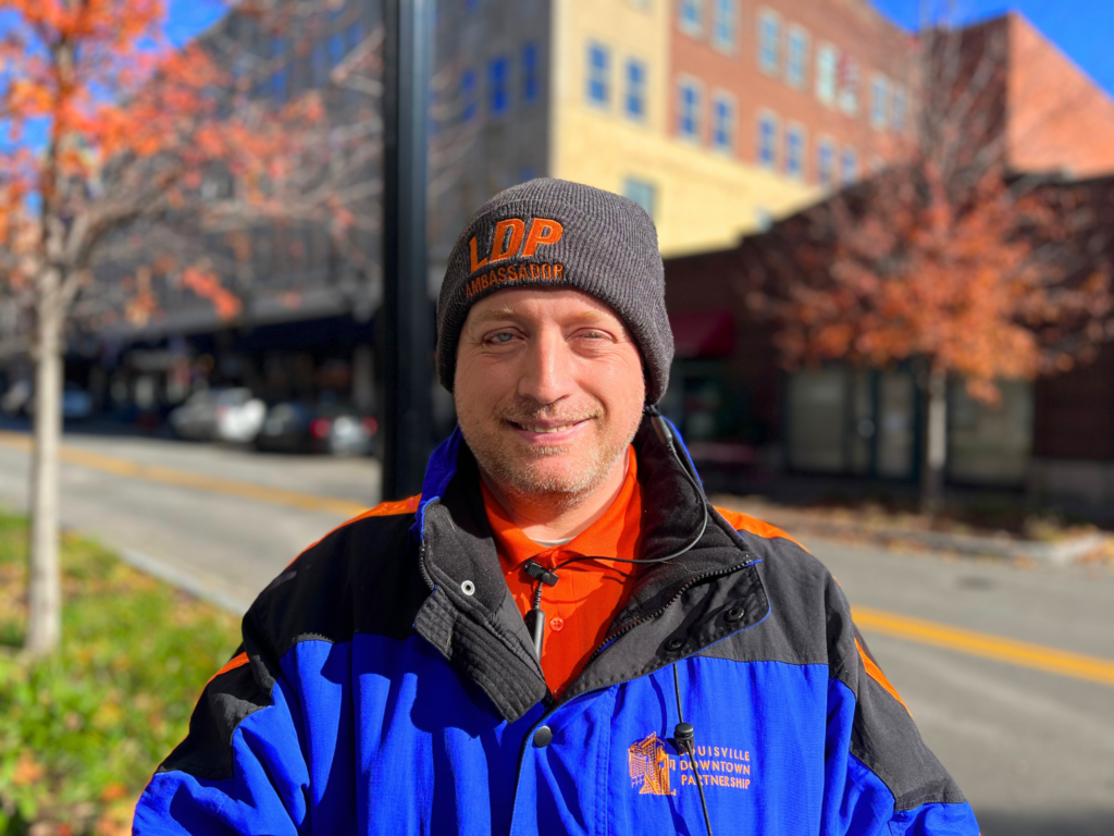 A man in uniform smiles as he stands on a sidewalk in Downtown Louisville.