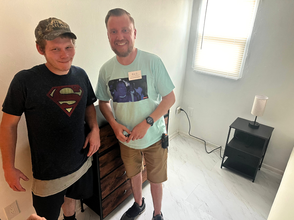 Outreach worker Eric stands next to a man he helped find housing for in his new room.